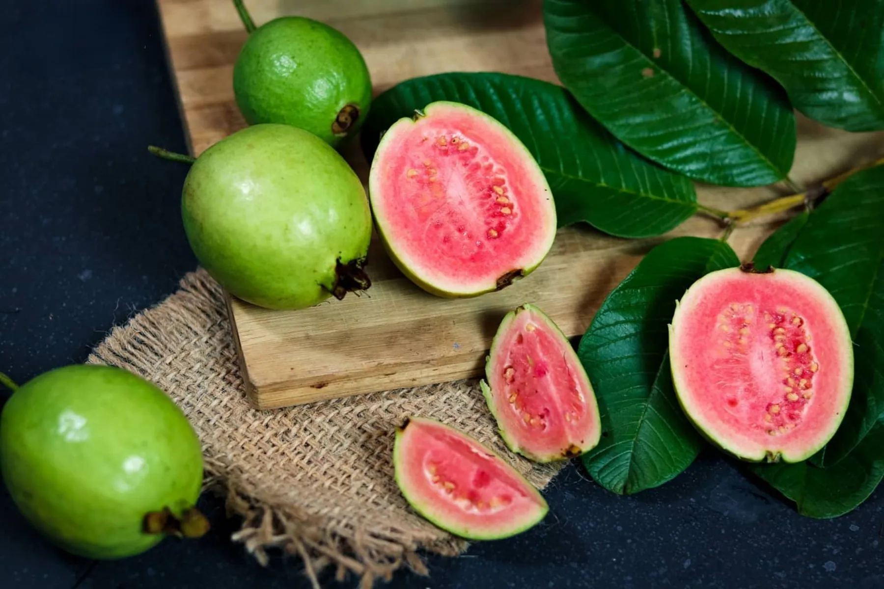 Whole and halved guavas showing their pink flesh, with leaves alongside
